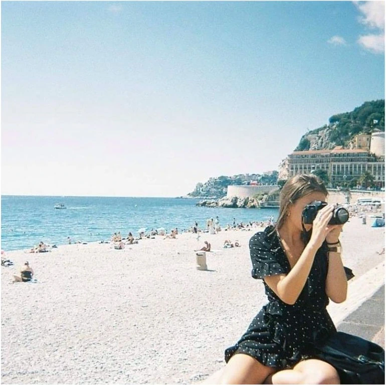Photographie de Camille Deceuninck assise de dos face à la mer, tenant un appareil photo reflex pour capturer un instant.