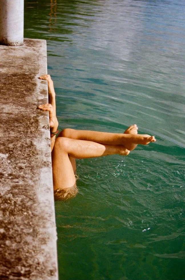 Femme partiellement immergée dont seuls les jambes et bras son visibles. Dos à la structure en béton, elle s'aggrippe à celle-ci, dans une eau aux tonalités verdâtres.