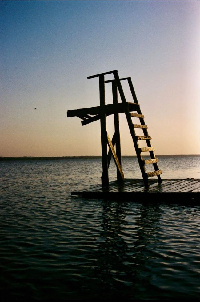 Bord de mer calme avec une structure en bois en silhouette sur un ponton, ciel aux tons chauds